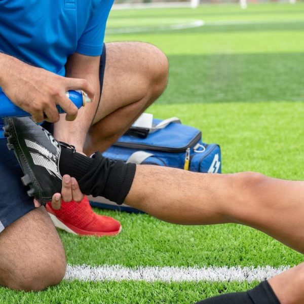 college athlete, football player injured lying on the field getting help from a friend