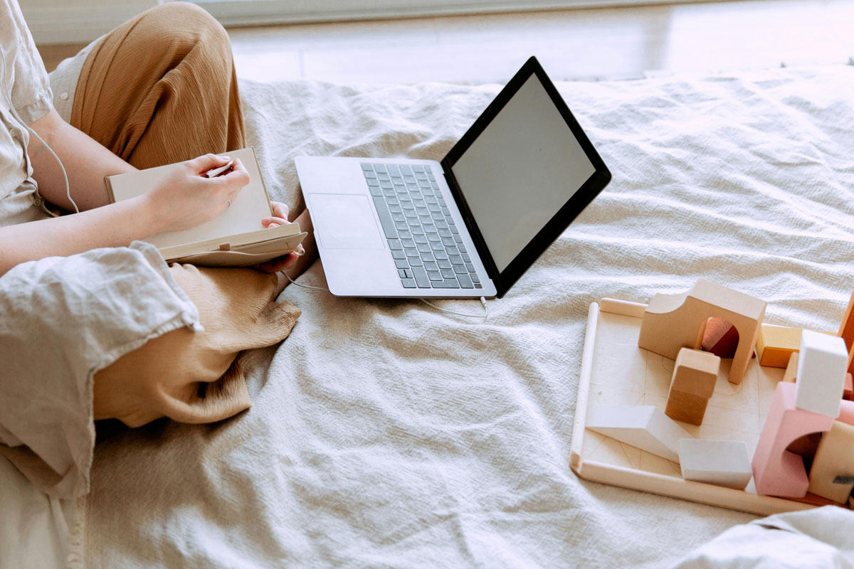 a person sitting on a bed with a laptop and a tray of wooden blocks