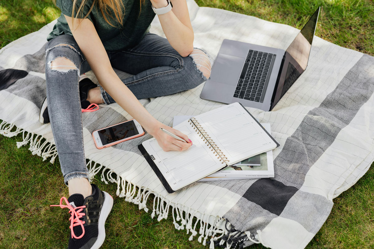 a person sitting on a blanket with a notebook and a laptop