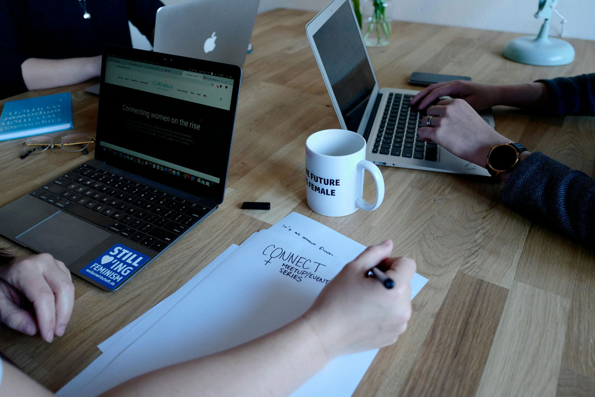 a person sitting at a table with laptops and a cup of coffee