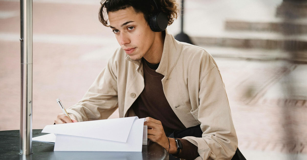 a man wearing headphones sitting at a table writing on paper