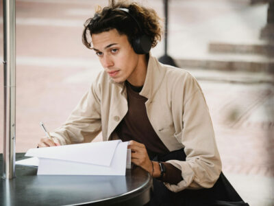 a man wearing headphones sitting at a table writing on paper