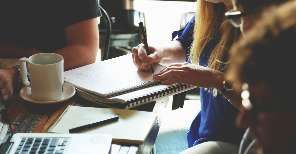 a group of people sitting at a table writing on a notebook